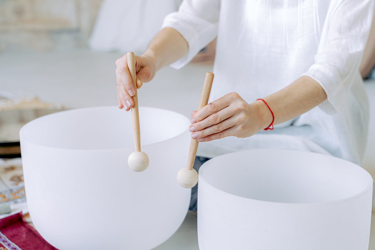 about-01 Hands playing crystal singing bowls with mallets, highlighting sound healing practice indoors.