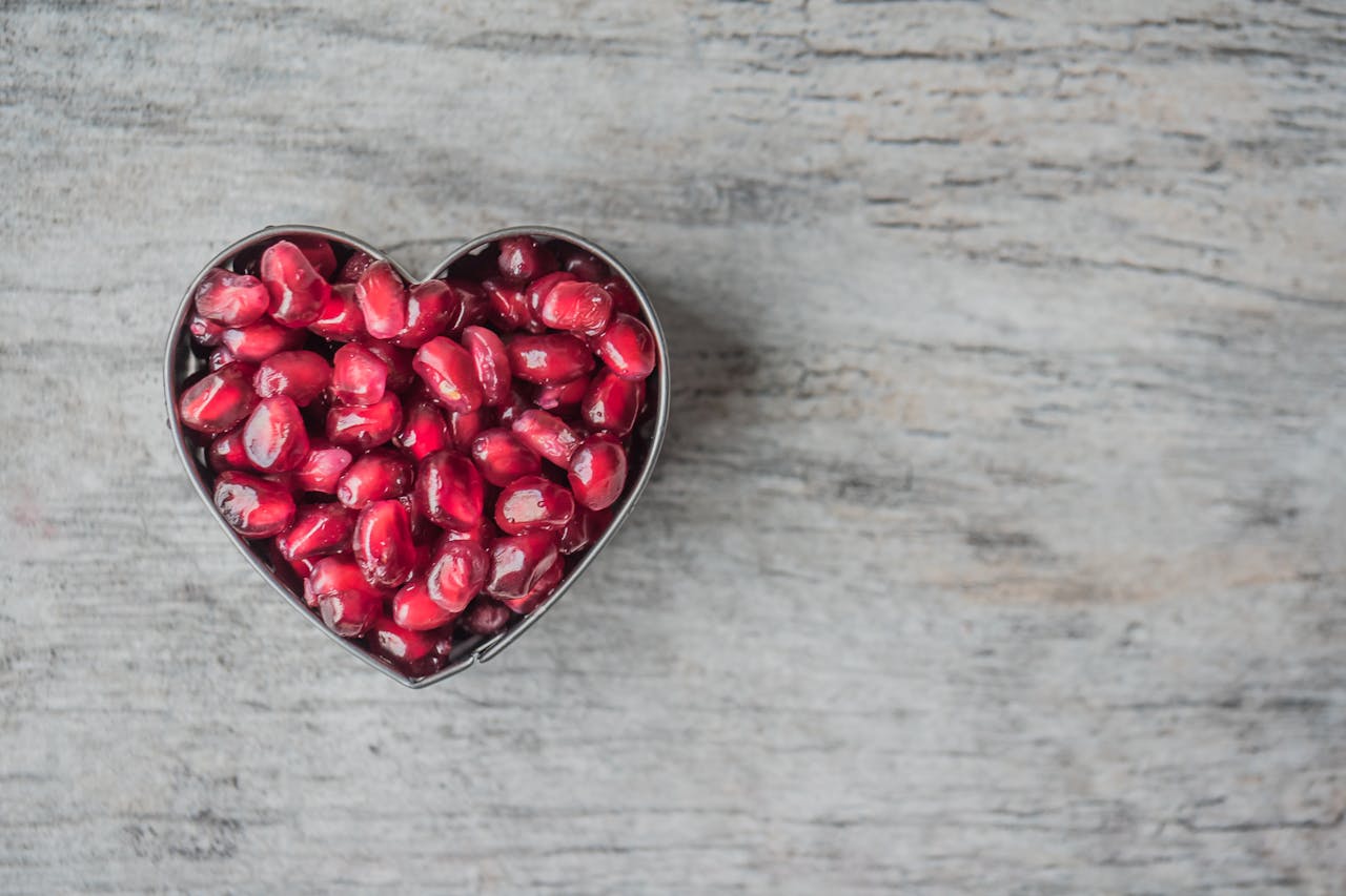 about-03 Delicious and juicy pomegranate seeds in a heart-shaped bowl on a wooden table.