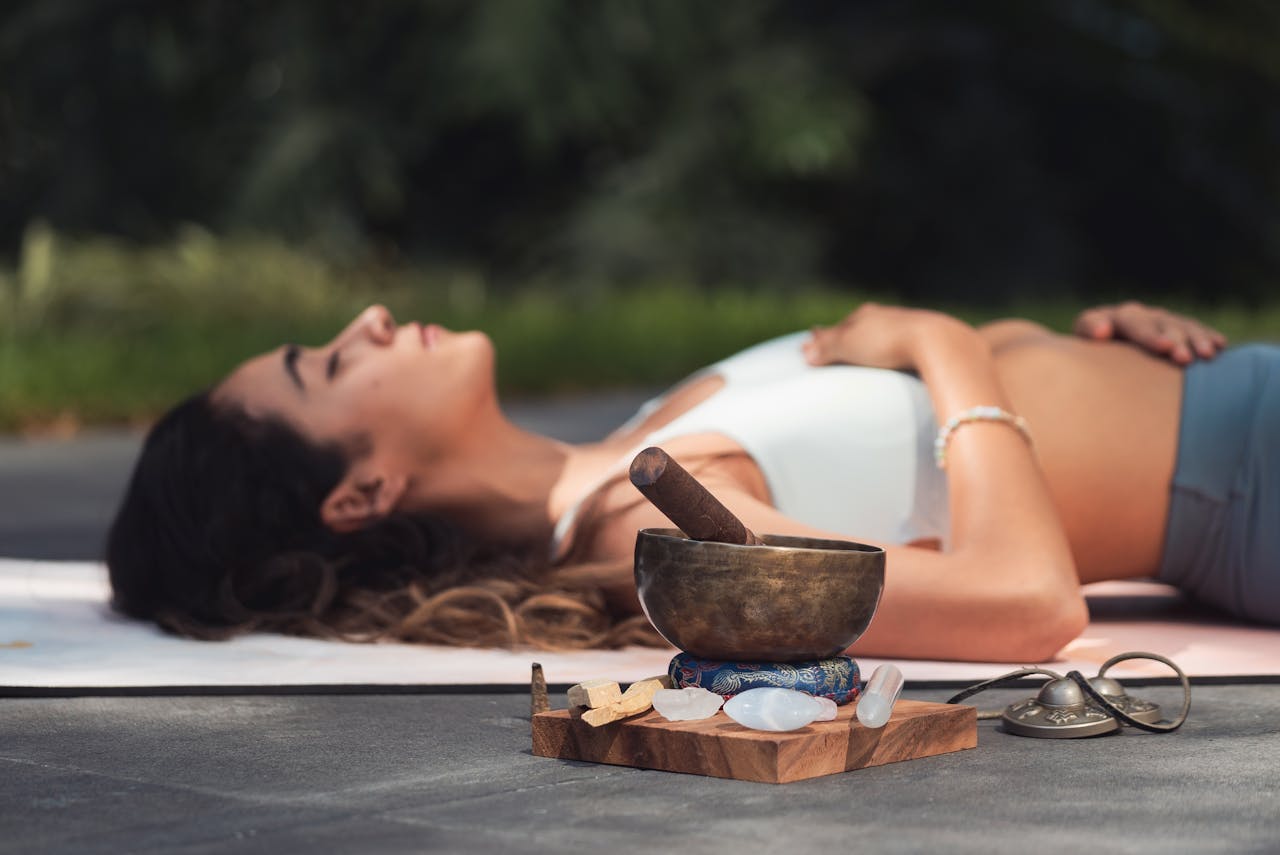 services-01 A woman practices relaxation with a singing bowl and crystals in an outdoor setting.